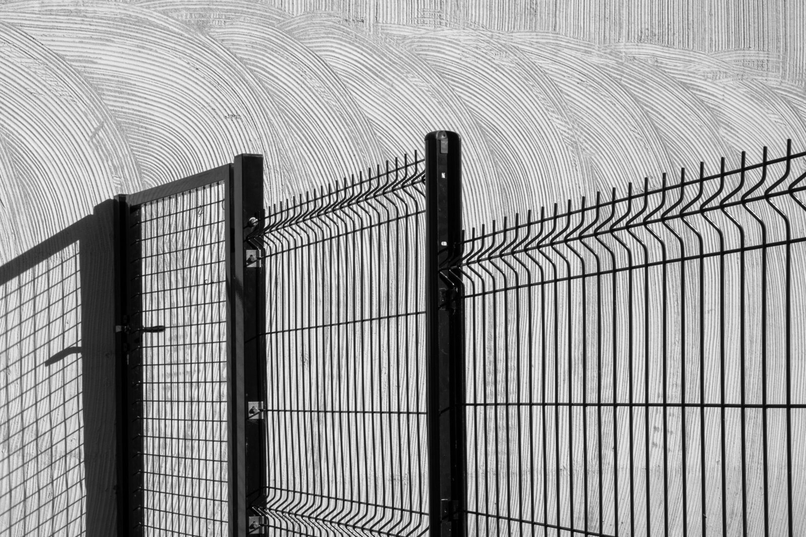 Artistic black and white photo of a wire fence casting shadows on a textured wall.